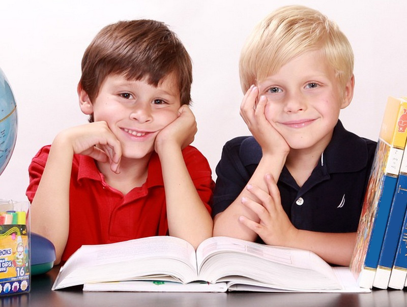 Zwei fröhliche Jungen mit Büchern am Schreibtisch