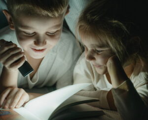 Zwei Kinder lesen mit Taschenlampe unter der Decke