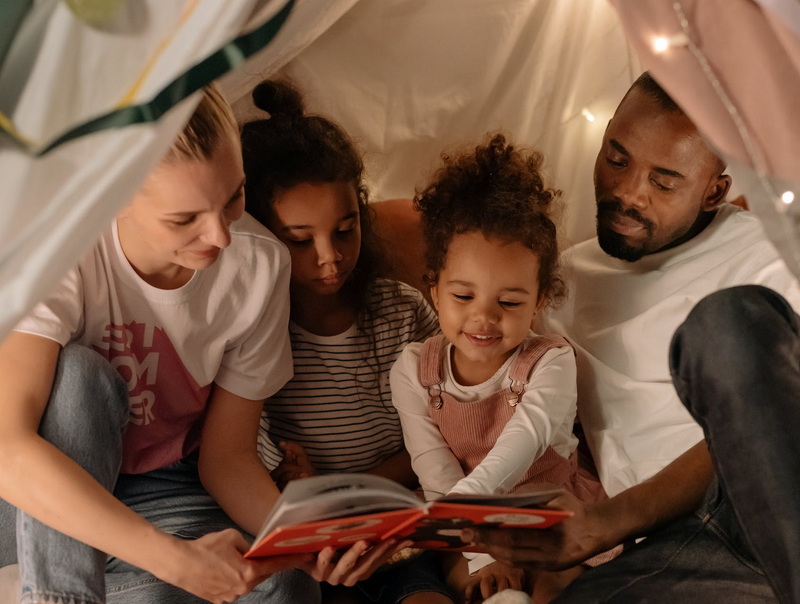 Zufriedene Eltern lesen mit ihren zwei Kindern unter einer Decke